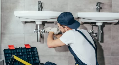 Back view of young professional plumber fixing sink in bathroom