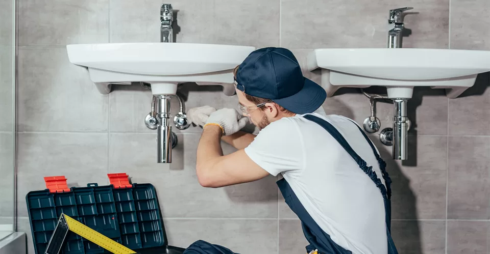 Back view of young professional plumber fixing sink in bathroom