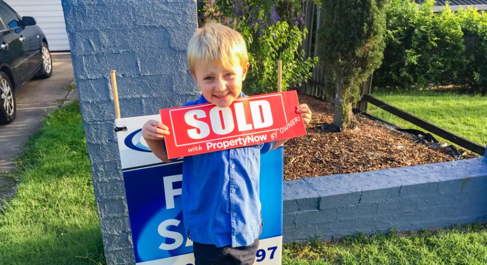 a little boy holding a SOLD sign