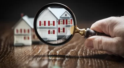 Hand Holding Magnifying Glass Up To Model Home