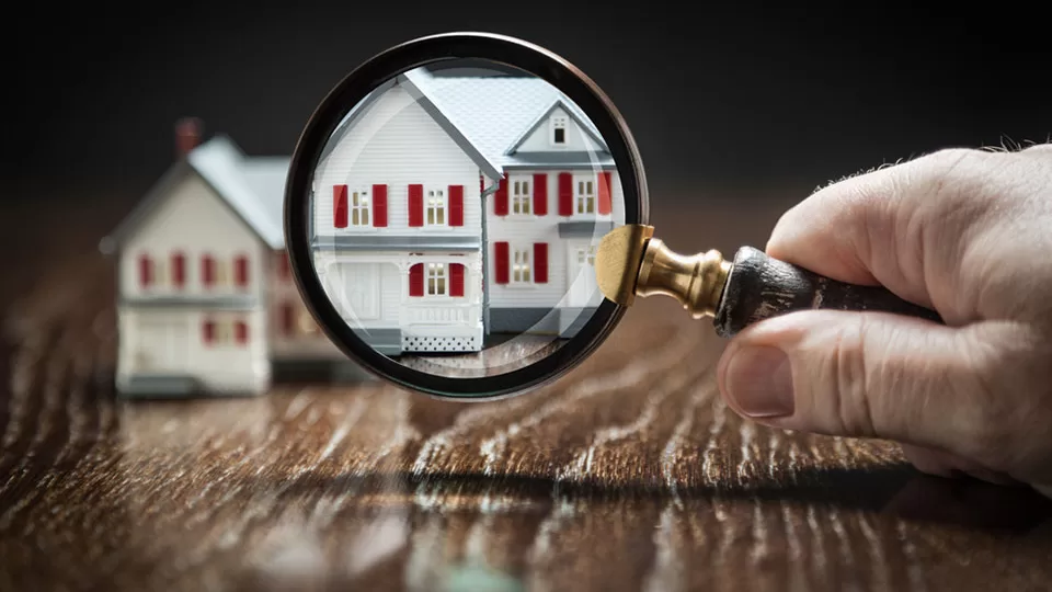 Hand Holding Magnifying Glass Up To Model Home