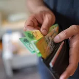 a man's hand holding a wallet and pulling out money from it