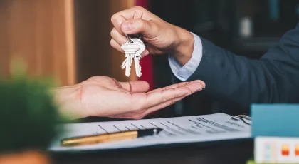 a hand giving a set of keys to another hand and a contract on the table