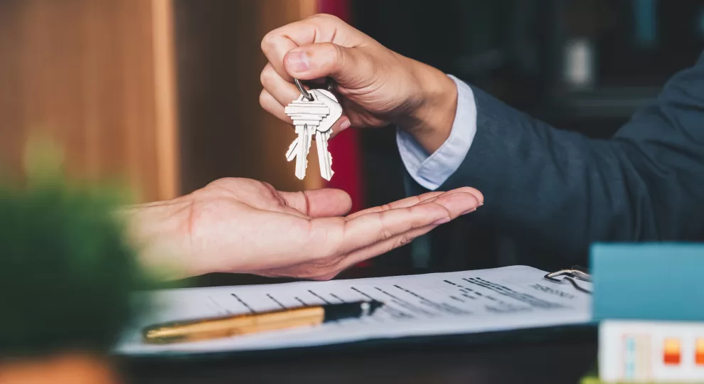 a hand giving a set of keys to another hand and a contract on the table