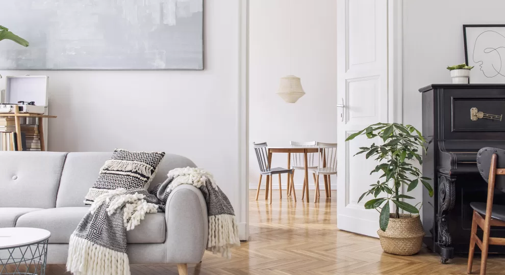 grey couch, an upright piano, and a smal dining table with three chairs