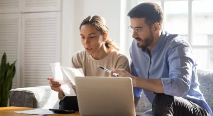 a woman and a man infront of a laptop while looking at pieces of paper