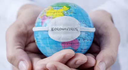a man's hands holding a small globe with the word 'coronavirus' on it