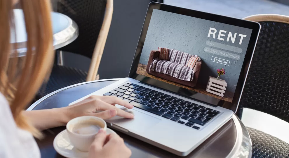 a woman in a coffee shop looking at a laptop with the word 'RENT' on the screen